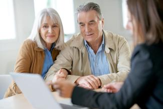 A retiree couple in a meeting with a professional. They are all looking at a laptop screen