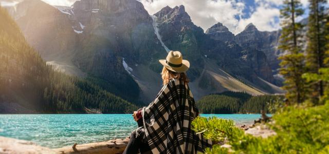 Woman sitting on a rock looking out at lake. In the distance is a large mountain range